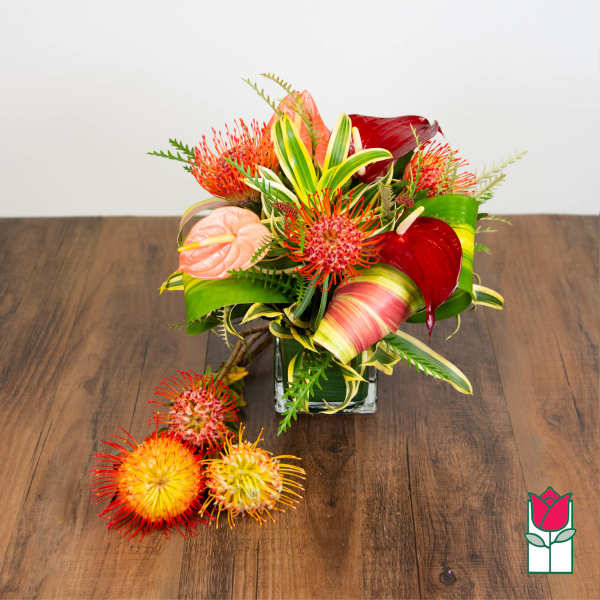 Tropical bouquet in a square glass vase with red and peach blooms