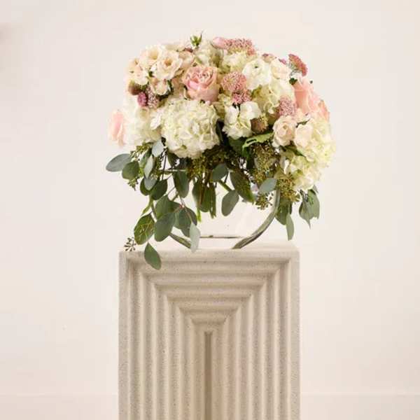 Blush and white floral arrangement on a pedestal with trailing greenery