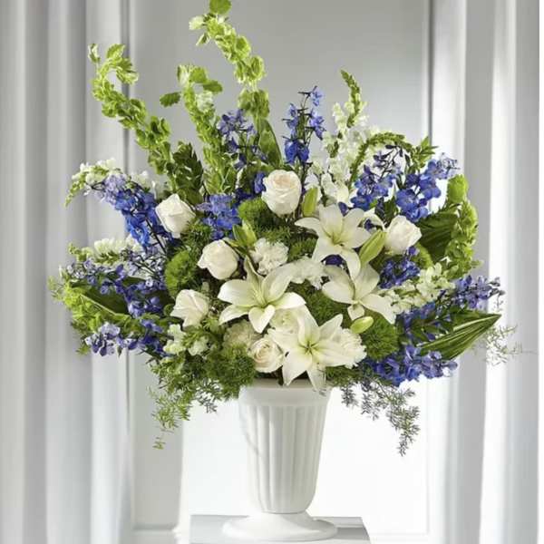 White lilies and blue flowers arranged in a white pedestal vase