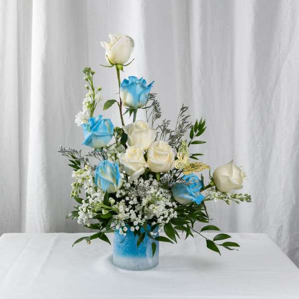 Blue and white roses arranged in a glass vase with greenery