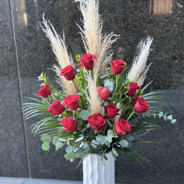 Tall arrangement of red roses with pampas grass in a white vase