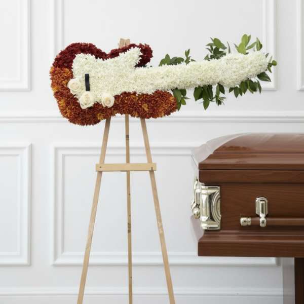 White and burgundy floral casket spray on an easel beside a wooden casket