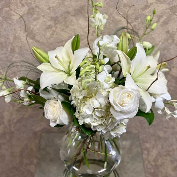 White lilies and roses arranged in a clear glass vase