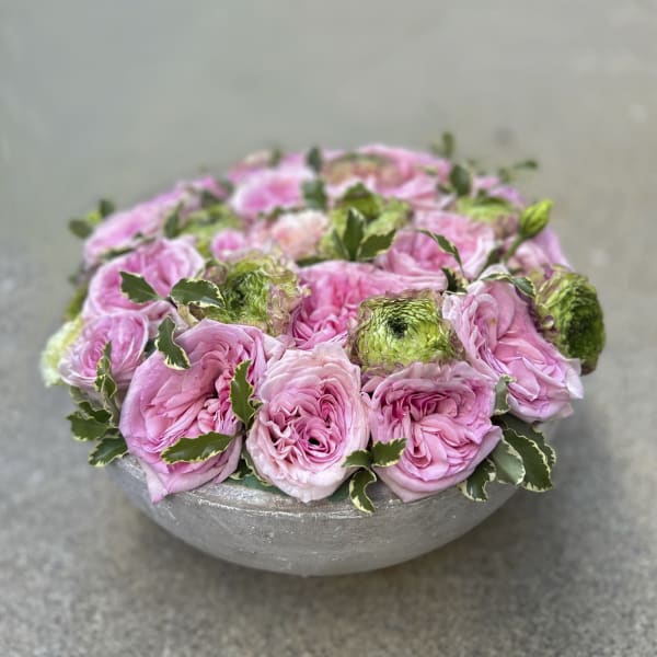Pink roses arranged in a low gray bowl with variegated foliage