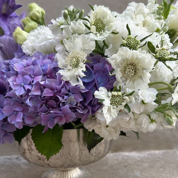 Purple and white floral arrangement in a decorative bowl vase