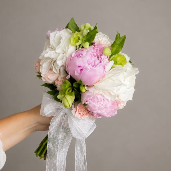 Handheld bouquet of pink and white peonies with a sheer white ribbon