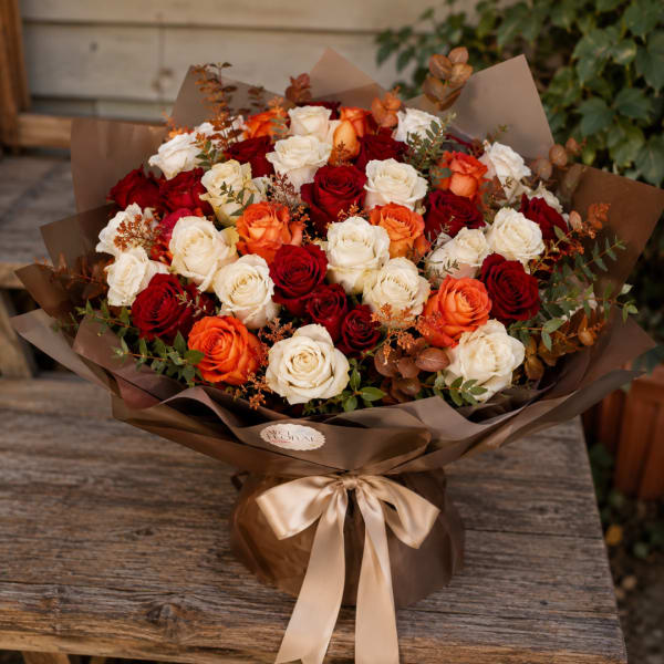 Bouquet of red, white, and orange roses wrapped in brown paper with a satin ribbon