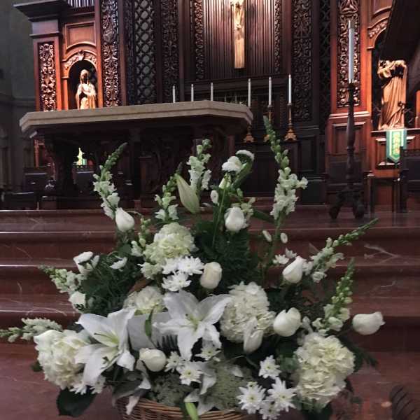 White floral arrangement in a wicker basket at an altar