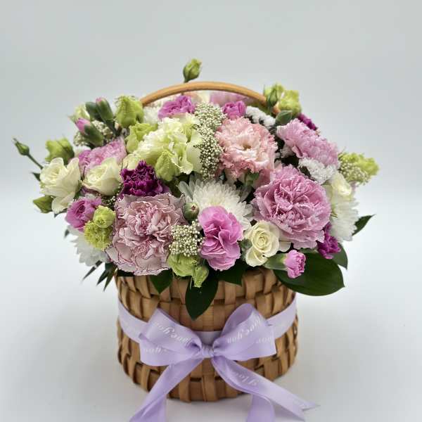 Pastel flower arrangement in a woven basket with a lavender ribbon