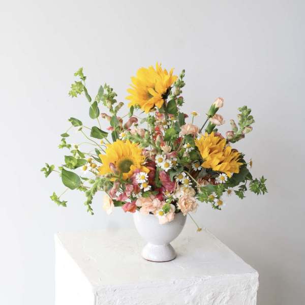 Mixed bouquet with yellow sunflowers and small pink and white flowers in a white vase