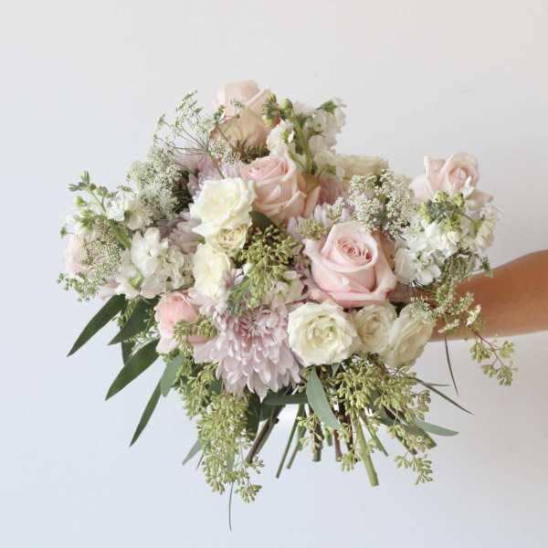 Handheld bouquet of pale pink and white flowers with trailing greenery