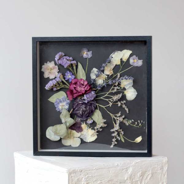 Framed pressed flower arrangement with purple, white, and pink blooms on a black background