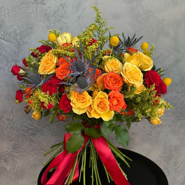 Bouquet of red, orange, and yellow roses with blue thistle and a red ribbon