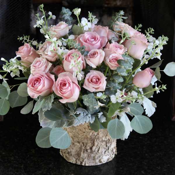 Pink roses arranged in a bark-covered vase with white filler flowers