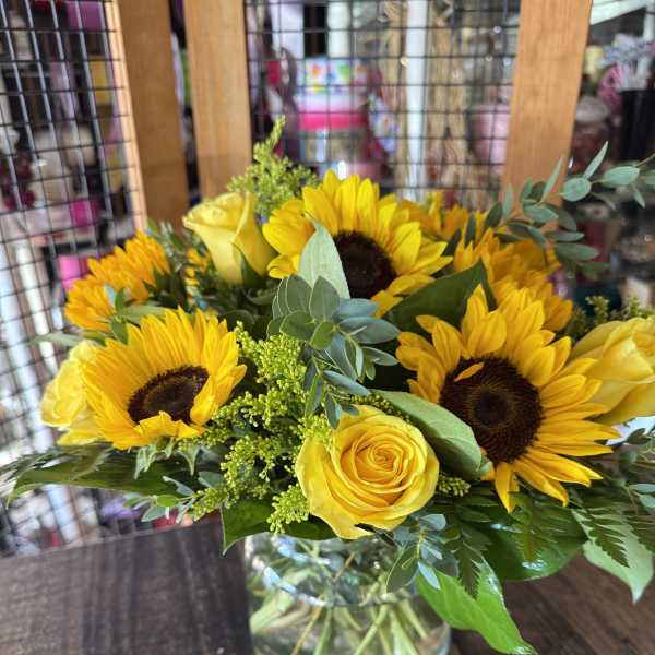 Yellow sunflowers and roses arranged in a glass vase