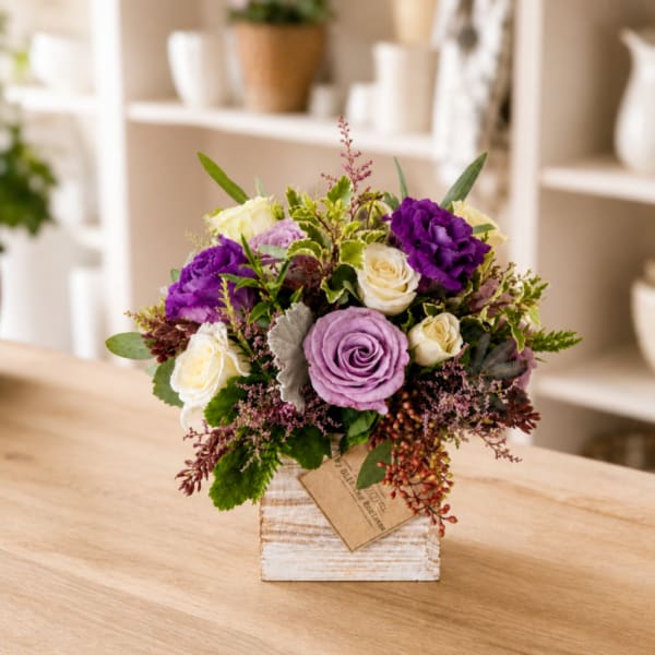Purple and cream rose arrangement in a rustic white vase