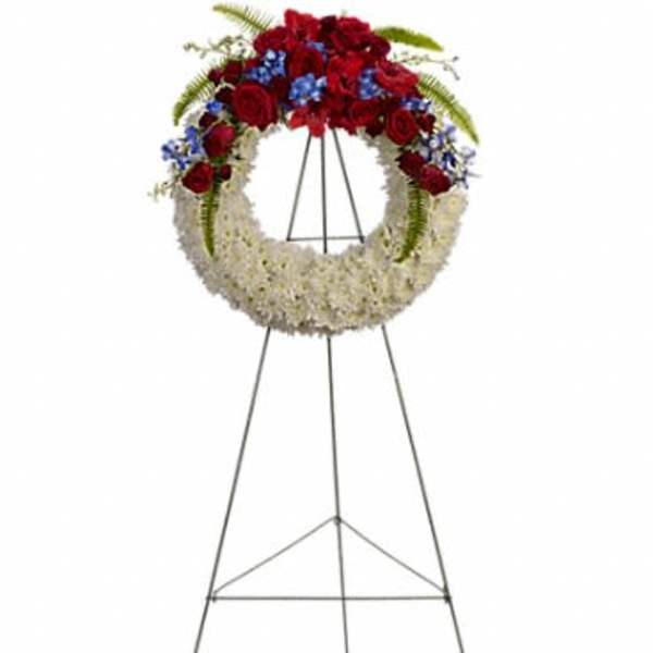 Standing round wreath of white flowers with red roses and blue blooms on a metal easel