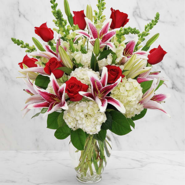 Bouquet of red roses, pink lilies, and white hydrangeas in a clear glass vase