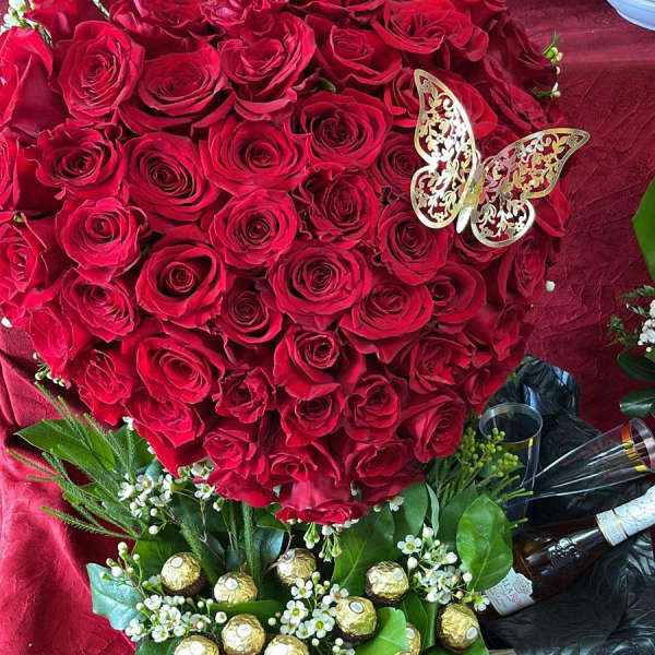 Heart-shaped bouquet of red roses with a butterfly pick and chocolates