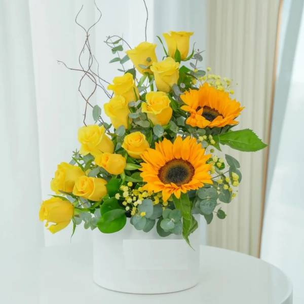 Yellow roses and sunflowers arranged in a white box.