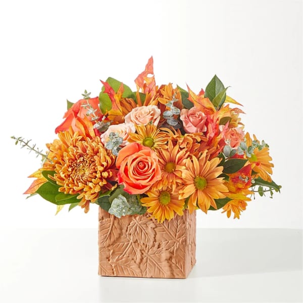 Orange and peach flower arrangement in a textured square vase