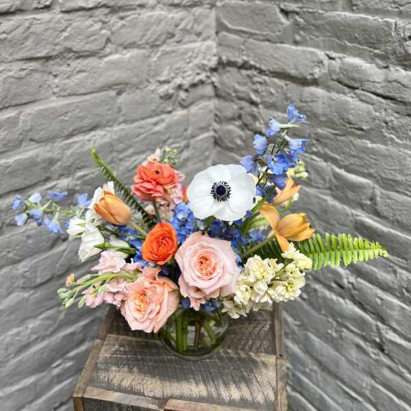 Mixed bouquet of roses, tulips, and blue flowers in a glass vase