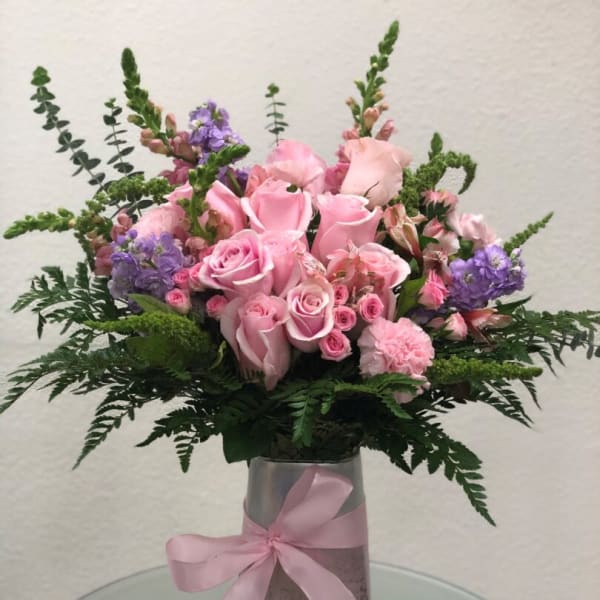 Pink roses and purple flowers arranged in a vase with a pink ribbon
