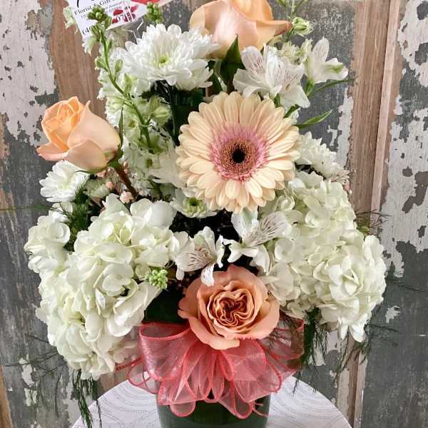 Peach roses and white flowers in a green vase with a pink ribbon