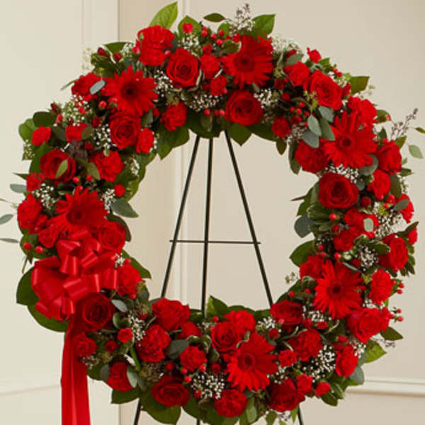 Red floral wreath on a black stand with a ribbon bow