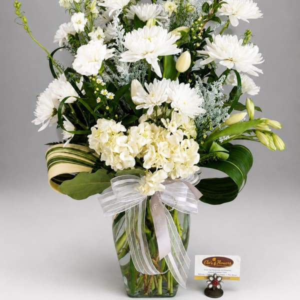 White floral arrangement in a glass vase with a ribbon bow