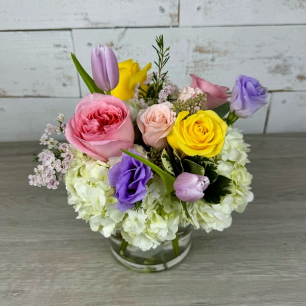 Mixed bouquet of roses, tulips, and lisianthus in a clear glass vase