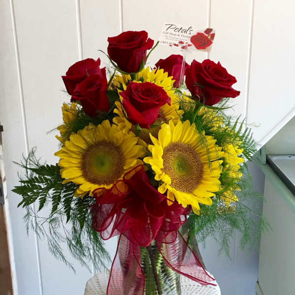Red roses and yellow sunflowers in a glass vase with a red ribbon