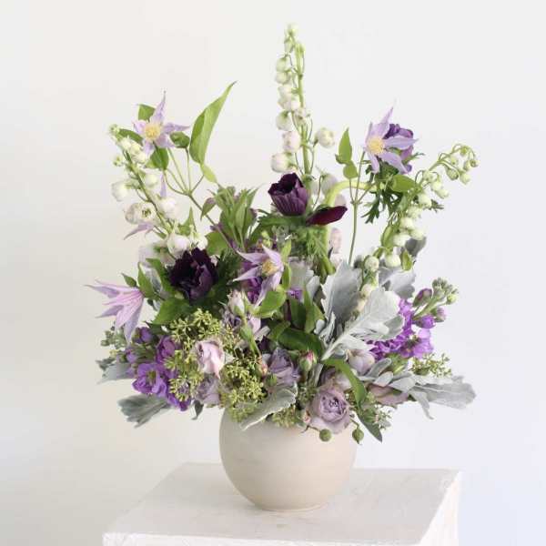 Purple and white floral arrangement in a round beige vase