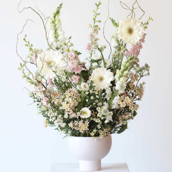 Tall floral arrangement with white daisies and pink blooms in a white vase