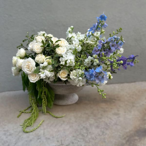 White roses and blue delphinium in a gray pedestal bowl