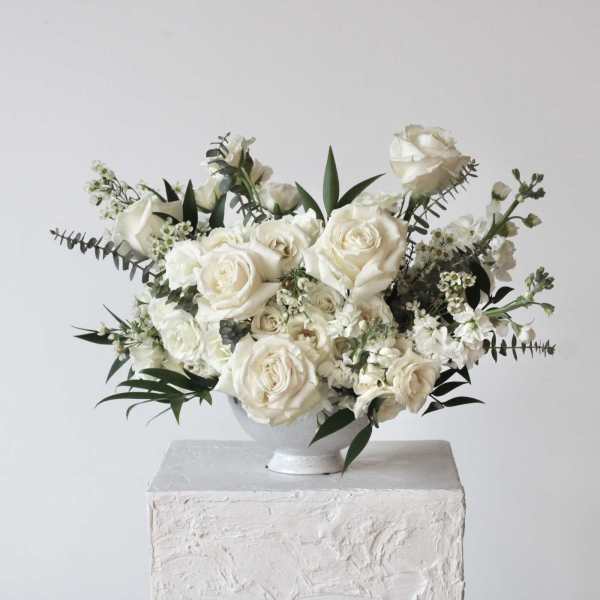 White rose arrangement in a white pedestal vase