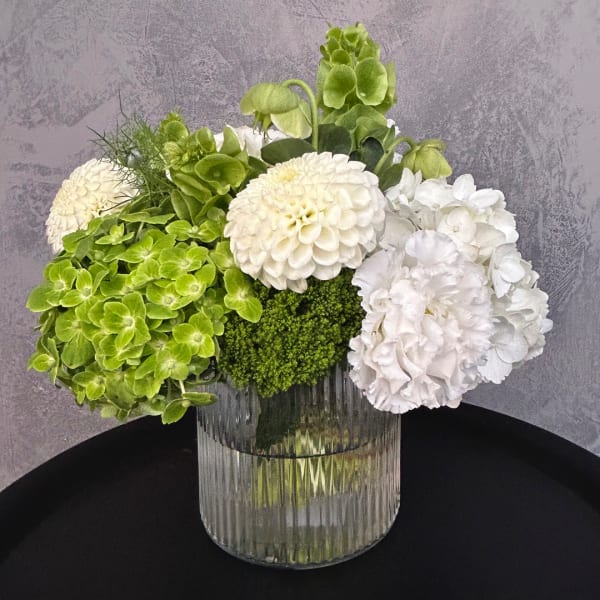 White and green floral arrangement in a ribbed glass vase