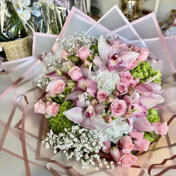 Pink roses and orchids arranged with white filler flowers in pastel wrap