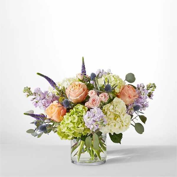 Bouquet of peach roses, hydrangeas, and lavender flowers in a glass vase