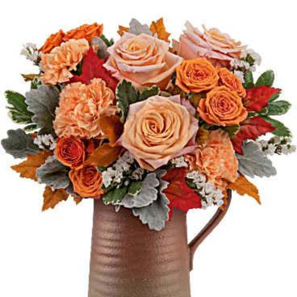 Orange and peach roses with carnations in a brown pitcher vase