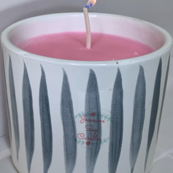 Pink candle in a white ceramic holder with a lit wick