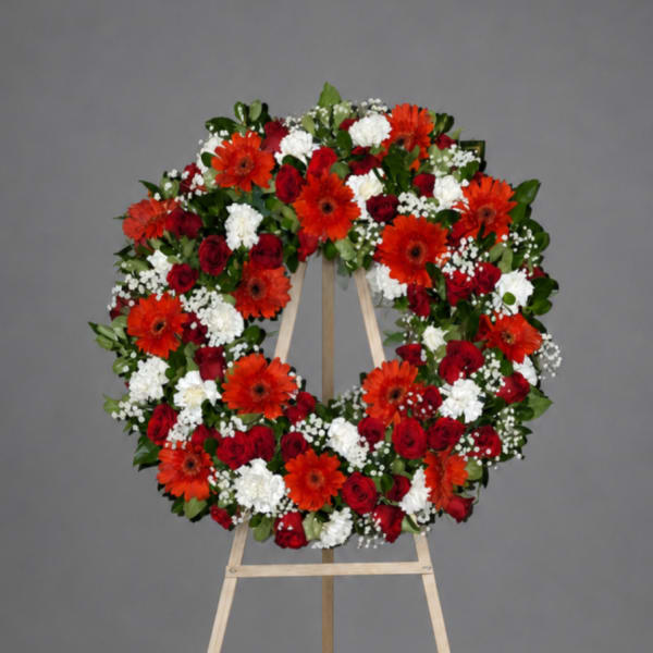 Circular floral wreath on a wooden easel with red, white, and orange flowers