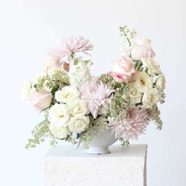 Soft pink and white floral arrangement in a white pedestal vase