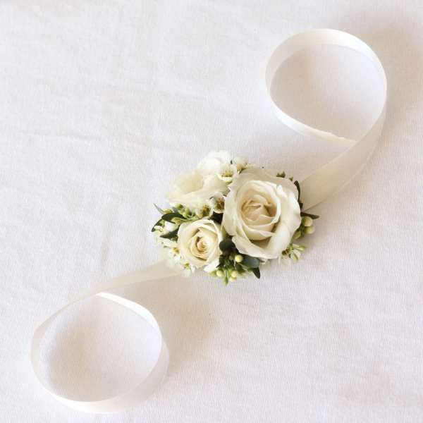 White rose wrist corsage with ribbon ties on a pale fabric background