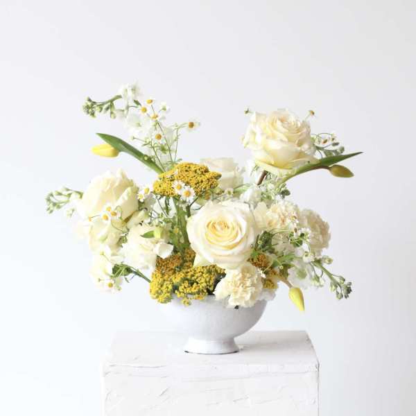 Cream roses and small white flowers arranged in a white bowl vase