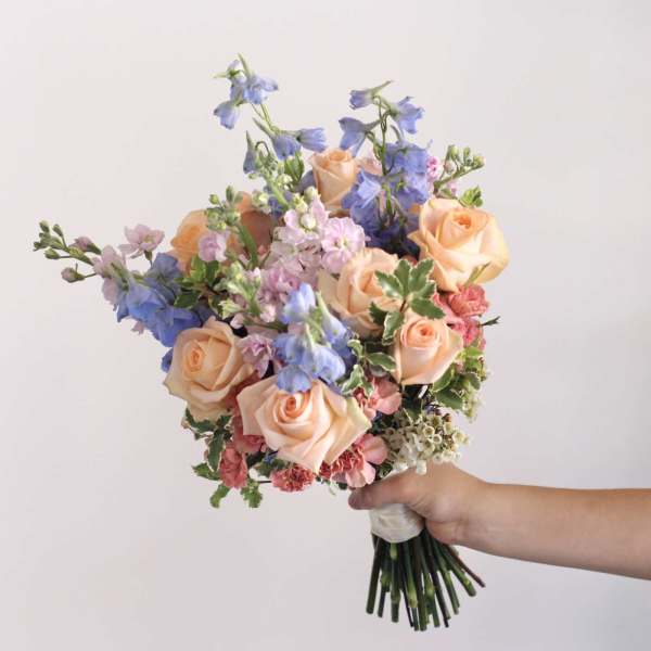 Handheld bouquet of peach roses, blue flowers, and pink blooms