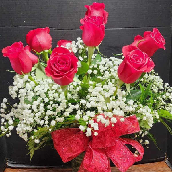 Red roses arranged in a glass vase with white baby's breath and a red ribbon