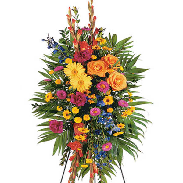 Tall standing spray of bright yellow, orange, pink, and blue flowers on an easel.
