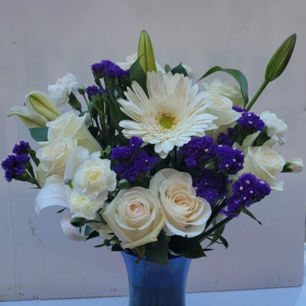 White roses and lilies with purple filler in a blue glass vase