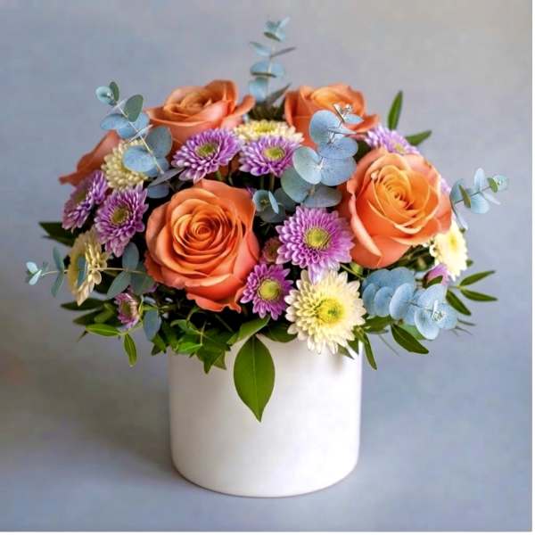 Orange roses and purple daisies in a white vase